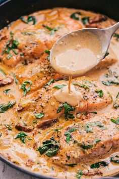 a pan filled with chicken and spinach covered in gravy being stirred with a spoon