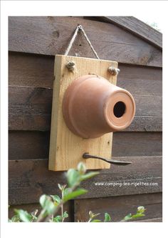 a clay pot hanging from a hook on a wooden wall with a garden tool attached to it