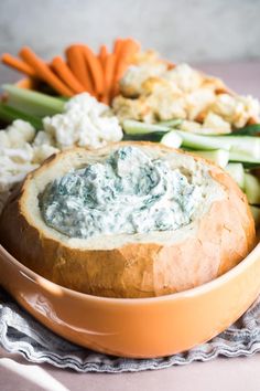 a bowl filled with dip and vegetables on top of a cloth next to a bread bowl