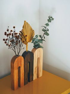 three wooden vases sitting on top of a yellow table next to plants and flowers