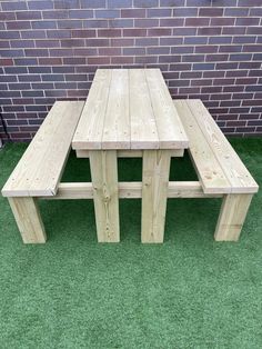 a wooden picnic table and bench sitting in front of a brick wall on green grass