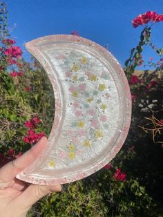 someone holding up a plastic plate with flowers on it in front of some pink flowers