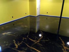 an empty room with yellow walls and black marble flooring in the center is a lamppost