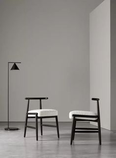 two chairs sitting next to each other in front of a wall with a lamp on it