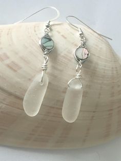 These elegant white sea glass and shell drop earrings feature pieces of sea glass that are beautifully matched in shape, size, and color. This is genuine sea glass that has been ocean-tumbled. For an idea of size please see photo 4. The abalone shell is wire wrapped. The ear wires are sterling silver. You can also purchase a matching necklace on an 18 inch sterling silver cable chain either separately or as a matching earring and necklace set in white (see sample photos using seafoam seaglass). White Glass Earrings With Ear Wire, White Recycled Glass Jewelry For The Beach, Handmade White Sea Glass Jewelry, Sea Glass Teardrop Earrings For Beach, Elegant Sea Glass Dangle Earrings, Red Sea Glass, Earring And Necklace Set, White Sea Glass, Sea Glass Earrings