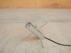 a metal object sitting on top of a cement floor next to a wire and plug