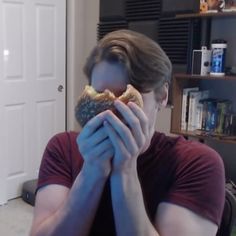 a man eating a donut with his hands in front of his face while sitting at a table