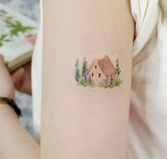 a small house tattoo on the left upper arm and right lower arm, with trees around it