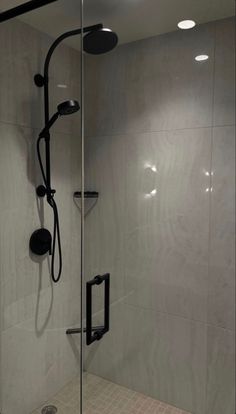 a walk in shower sitting next to a white tiled wall with black fixtures on it