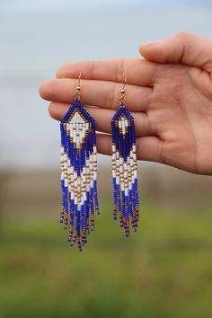 a hand holding some kind of blue and white beaded earrings on it's fingers