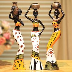 three figurines are standing on a table with flowers in front of them and one is holding a vase