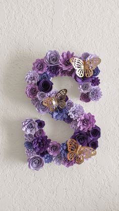 the letter e is made up of purple flowers and butterfly shapes on a white wall