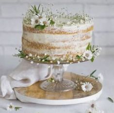 a three layer cake sitting on top of a wooden table next to white flowers and greenery