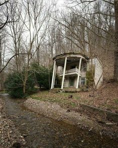 an old abandoned house in the woods near a stream and trees with no leaves on it