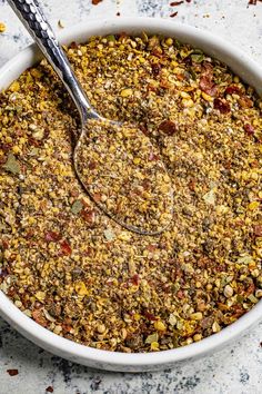 a white bowl filled with granola on top of a marble counter next to a spoon