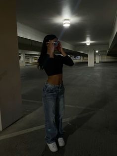 a woman standing in an empty parking garage taking a photo with her cell phone while wearing jeans