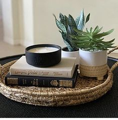 a wicker tray with two books and a candle on it next to a potted plant