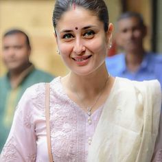 a woman wearing a white sari and smiling at the camera with other people in the background