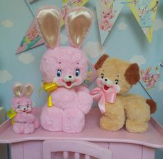 three stuffed animals sitting on top of a pink table next to bunnies and flags