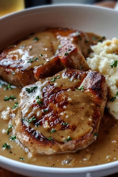 some meat and gravy in a white bowl on a table with mashed potatoes