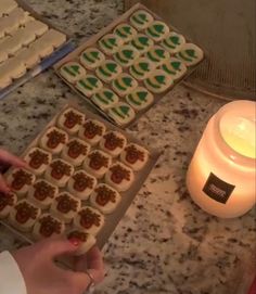 someone is decorating cookies with icing on the counter next to a lit candle