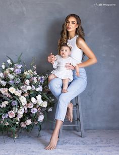 a woman sitting on a stool holding a baby in front of a bouquet of flowers