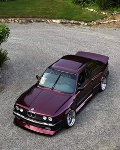 a purple car parked in the middle of a parking lot next to some bushes and trees