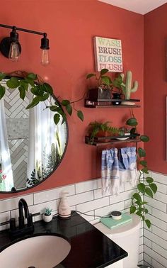 a bathroom with a sink, mirror and plants on the wall above it's toilet