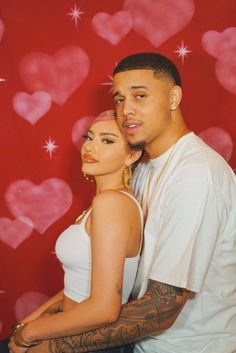 a man and woman posing for a photo with hearts on the wall in the background