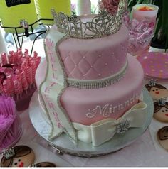 there is a pink and white cake with tiara on it, surrounded by cupcakes