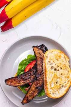 there is a sandwich with meat and vegetables on the plate next to two yellow pencils