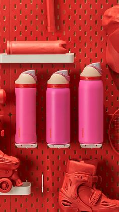 three pink water bottles sitting on top of a red wall next to tennis rackets