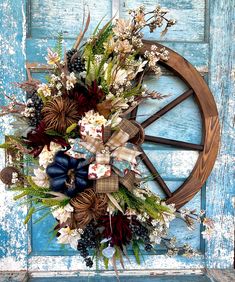 a wreath on the front door of a blue wooden building with an old wagon wheel