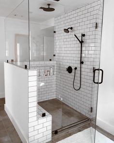 a white tiled bathroom with glass shower doors and black fixtures on the wall, along with a walk in shower