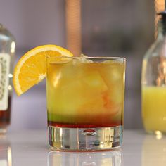 a close up of a drink with an orange slice on the rim and two bottles in the background