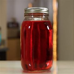 a jar filled with red liquid sitting on top of a table next to a straw