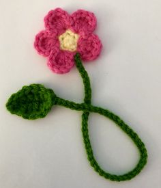 a crocheted pink flower with green stems on a white surface, ready to be made into an ornament