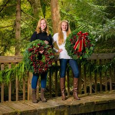 two women holding wreaths standing on a bridge in front of christmas wreaths and trees