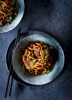 two bowls filled with noodles and vegetables next to chopsticks on a table top