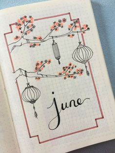 an open notebook with the word june written in black ink and flowers on it, next to a pen