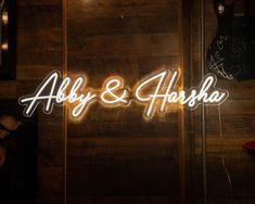 the neon sign for alby and ahohha is lit up in front of a wooden wall