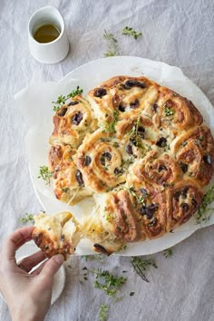 a person holding a piece of bread with olives and cheese on it next to a cup of tea