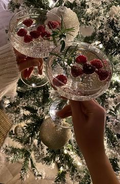 two wine glasses with raspberries in them are sitting on a table next to a christmas tree