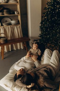 a woman laying on top of a bed next to a christmas tree with a baby in her lap