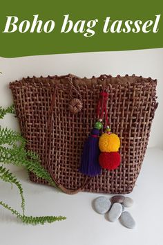 a woven bag with tassels on it next to some rocks and green plants