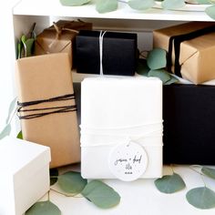 several wrapped presents sitting on top of a table next to eucalyptus leaves and white boxes