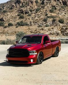 a red truck is parked in front of a mountain and sand area with hills behind it