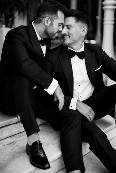 two men in tuxedos are sitting on steps and one is holding his arm around the other man's shoulder