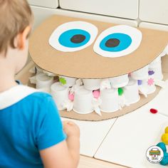 a young boy is looking at a cardboard monster made out of toothpaste tubes