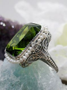 Simulated Green Peridot Ring Description Rectangle Seed Pearl Leaf Design#234 MADE TO ORDER This is a stunning Victorian reproduction in sterling silver filigree with a simulated green peridot rectangle stone... The stunning stone is 18mm by 13mm...The ring sits 21mm NS by 19mm EW... The inside of the band is marked 925 for sterling. Notice the beautiful craftsmanship of the silver filigree setting and band. The small natural pearls are 2mm wide... The ring is 9mm off the finger This is an ornat Leaf Filigree, Filigree Pendant Necklace, Antique Style Rings, Pearl Design, Green Gems, Peridot Ring, Sterling Silver Filigree, Peridot Gemstone, Green Peridot